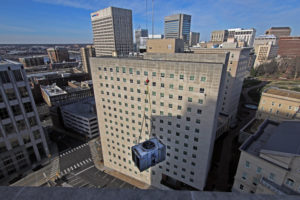 crane lifting HVAC equipment onto skyscraper downtown city