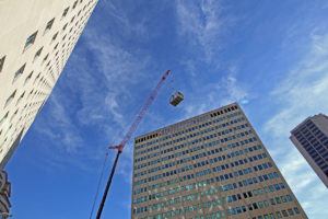 street view of crane lifting HVAC equipment onto a skyscraper